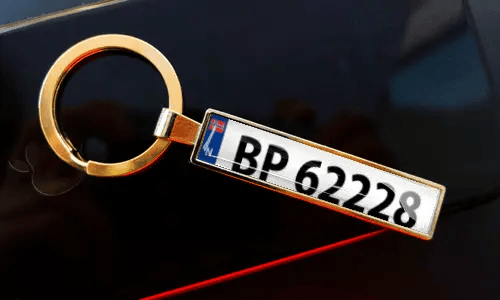 License plate keychain attached to keys in pocket with car in background