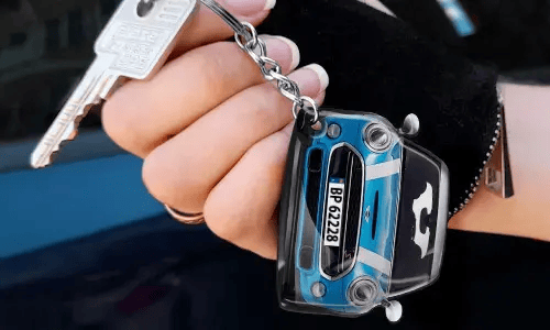Hand die een sleutelhanger in de vorm van een blauwe auto vasthoudt met een gedetailleerd frontontwerp