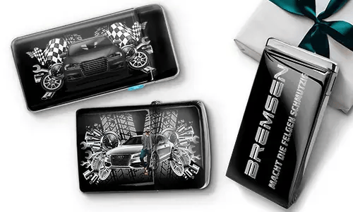 Car-themed wallets featuring sleek cars, checkered flags, and tire patterns on a black background. Beside them, a black gift box with silver text.