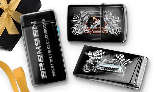Sleek black lighters with car-themed designs. One features a family in a car; another shows a blue car with checkered flags. Gift box with gold ribbon nearby.