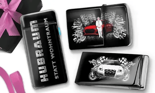 Drei Zigarettenetuis in Schwarz und Silber mit dynamischen Auto-Grafiken. Eines trägt die Aufschrift „Hubraum statt Wohntraum“, während die anderen Rennmotive zeigen.