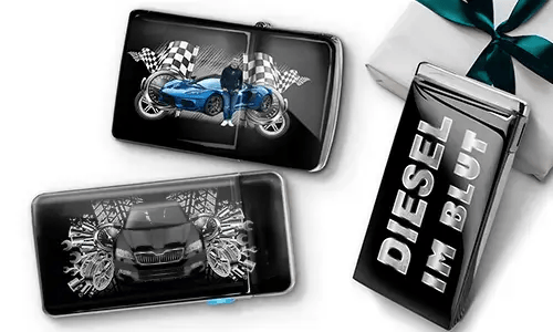 Two sleek black lighters featuring car themes, one with a blue car and checkered flags, another with a red car and gears. A third lighter reads 'DIESEL IM BLUT'. Gift-wrapped in the background.