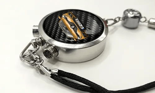 Round car key fob with carbon fiber face, buttons labeled LOCK and UNLOCK, braided black cord attached