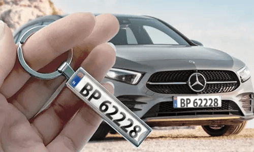 Tegneserie-nummerpladenøglering holdt i hånden med matchende bilnummerplade i baggrunden