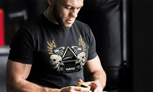 Black T-shirt with graphic of car, skulls, pistols, golden wings, and starry triangle background